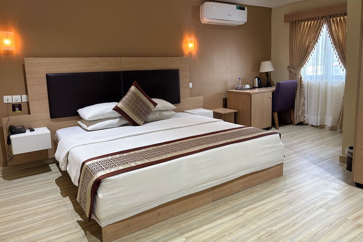 Ein Hotelzimmer mit einem großen Bett, Nachttischen, einem Schreibtisch, einem Stuhl, einer Klimaanlage und einem Fenster mit Vorhängen.