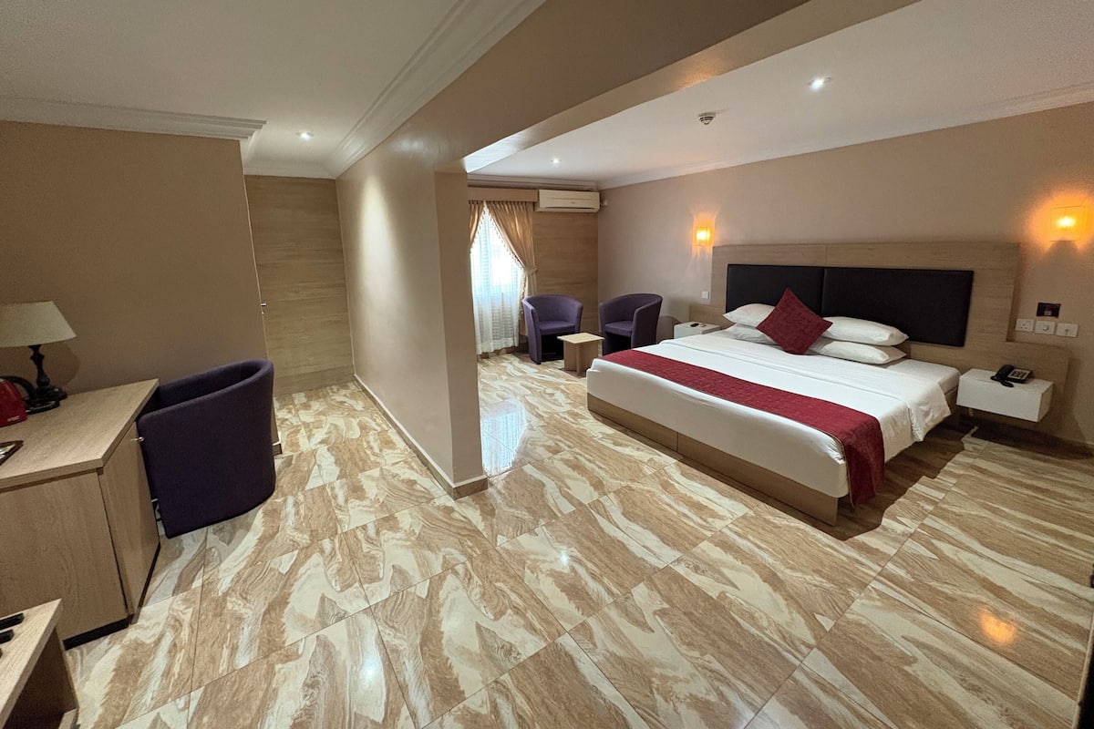 Ein Hotelzimmer mit einem großen Bett, einem Schreibtisch, zwei Stühlen, einem Nachttisch und einer Lampe.