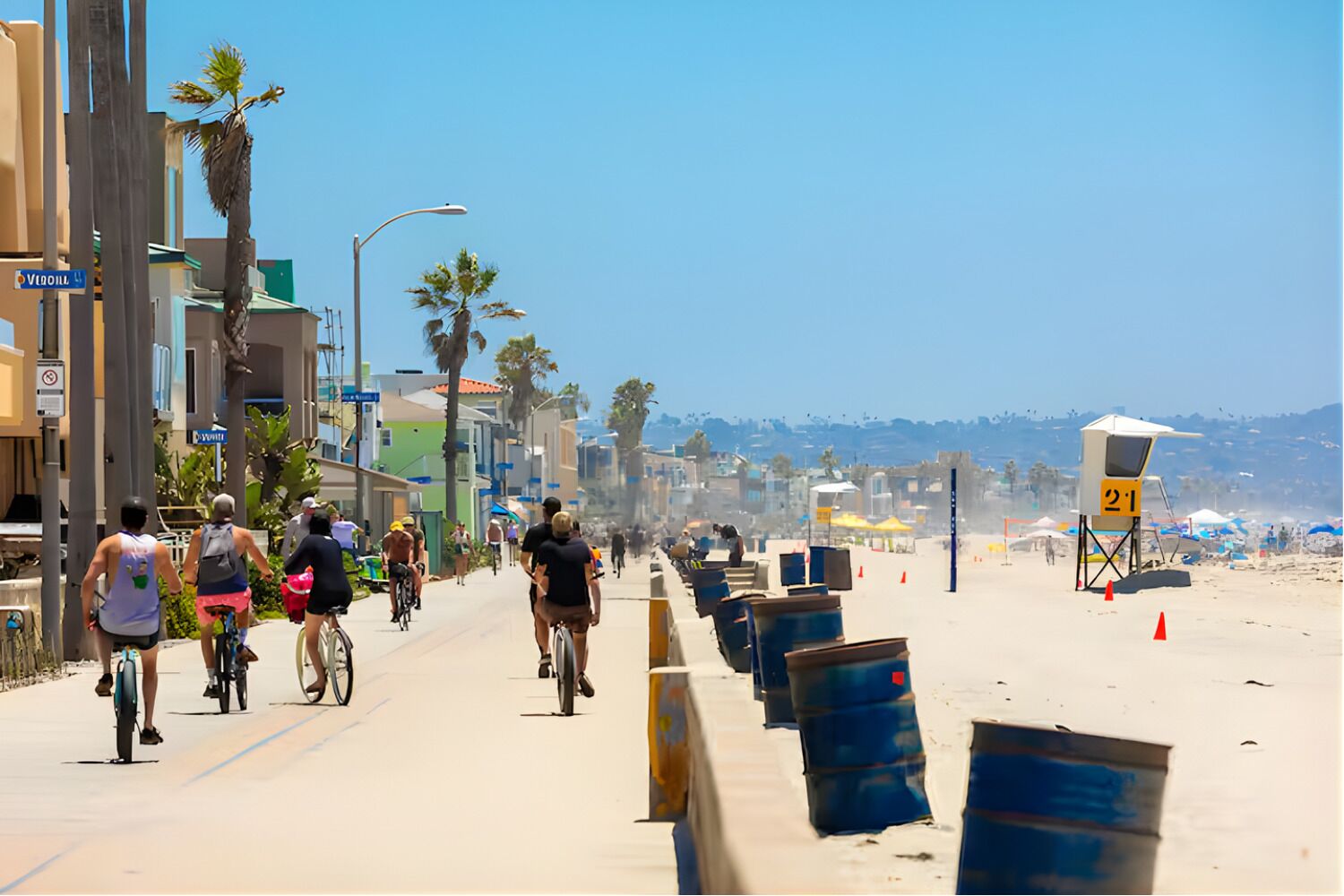 Een straat aan het strand met fietsers, palmbomen en strandparasols.