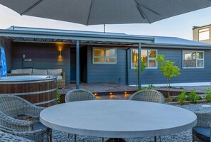 Un patio al aire libre con una mesa redonda y sillas de mimbre, un jacuzzi y un área de estar techada con vistas a la casa.