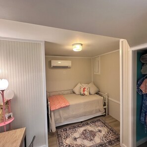 Una camera da letto piccola con un letto, un condizionatore d'aria, un comodino e un tappeto decorato.