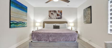 Um quarto com uma cama, ventilador de teto e obras de arte nas paredes.