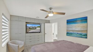 Quarto com cama, ventilador de teto, televisão, uma cadeira e um quadro.