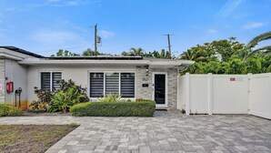 Uma casa moderna de dois andares com um caminho de entrada pavimentado, porta de garagem branca e um jardim frontal bem cuidado com diversas plantas.