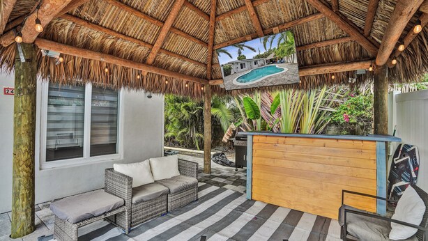 Área de estar coberta ao ar livre com móveis de vime, um balcão de madeira e vista para a piscina.