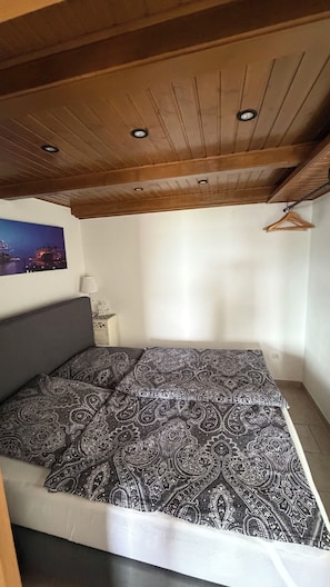 Ein Schlafzimmer mit einem Bett, einer Holzbalkendecke, einer Wandlampe und einem gerahmten Bild.