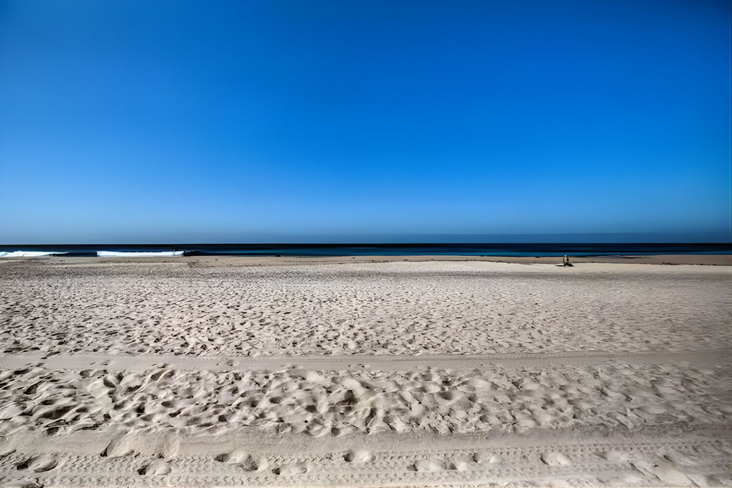 A wide sandy beach with footprints leading towards the ocean.