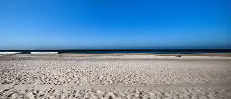 A wide sandy beach with footprints leading towards the ocean.