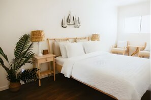Ein ordentlich eingerichtetes Schlafzimmer mit einem hölzernen Bett, weißer Bettwäsche, zwei Nachttischen mit Lampen, einer großen Topfpflanze und einem dekorativen Wandelement.
