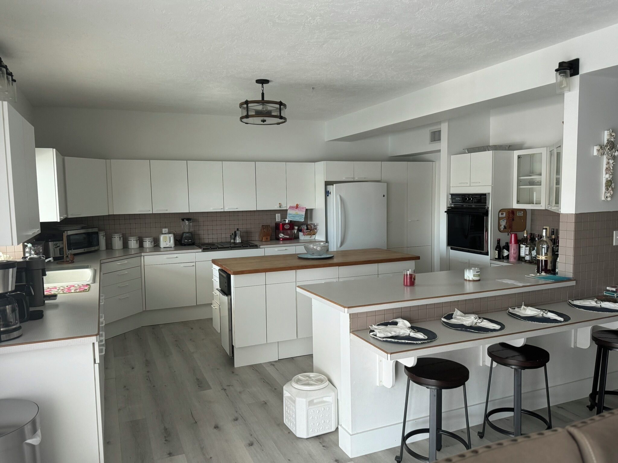 A modern kitchen with white cabinets, a central island with stools, a built-in oven, and a microwave.