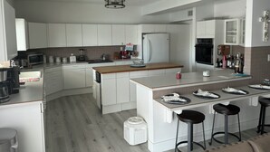 Eine moderne Küche mit weißen Schränken, einer zentralen Kochinsel mit Barhocker, einem eingebauten Backofen und einer Mikrowelle.
