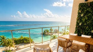 Ein Balkon mit Meerblick, Korbmöbel, ein kleiner Tisch mit einer Pflanze und ein Kissen mit Aufdruck.