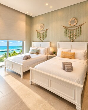 A hotel room with two beds, a view of the ocean, and decorative wall hangings.