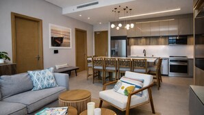 Ein modernes Wohnzimmer mit Sofa, Couchtisch und Sessel, ein Essbereich mit Stühlen und eine Küche mit Geräten.