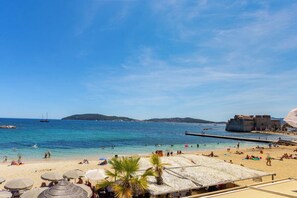 Ein Strand mit klarem, blauem Wasser, Sonnenschirmen und Menschen.