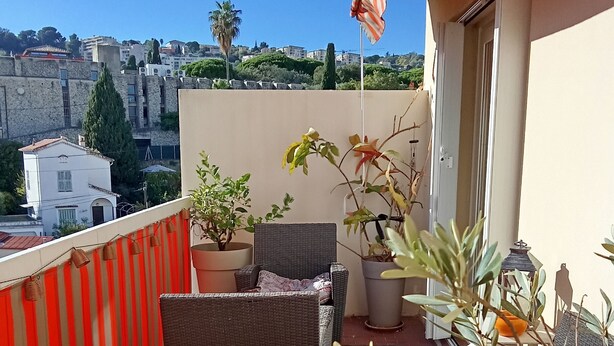 A balcony with wicker furniture, potted plants, and a view of buildings in the background. - Sea-view terrace. 2mn from the streetcar, very well equipped, Pets welcome (Nice)