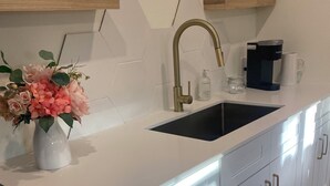 A modern kitchen with a white countertop, stainless steel cabinets, a gold faucet, and a coffee maker. - Modern One bedroom Near Bishops Arts District (Dallas)