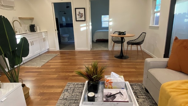 A spacious living area with a white sofa, a coffee table with a plant, and a dining area with a small table and chairs. - Modern One bedroom Near Bishops Arts District (Dallas)