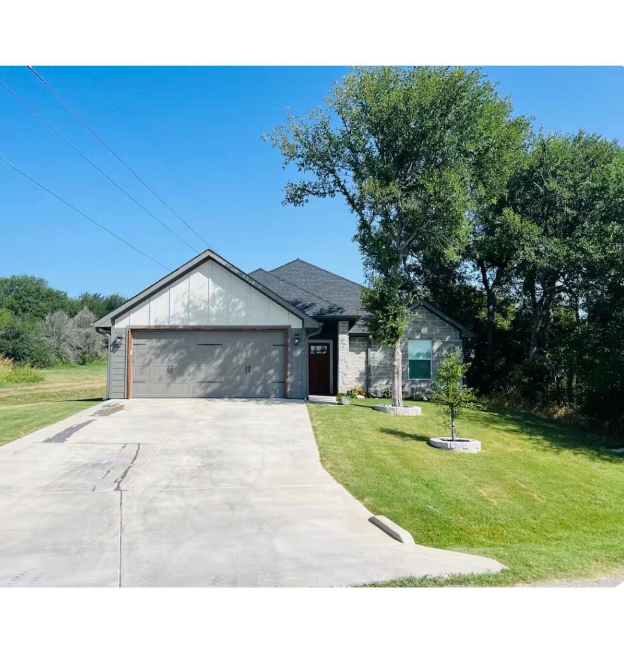 A single-story house with a garage, a front lawn, and a small tree.