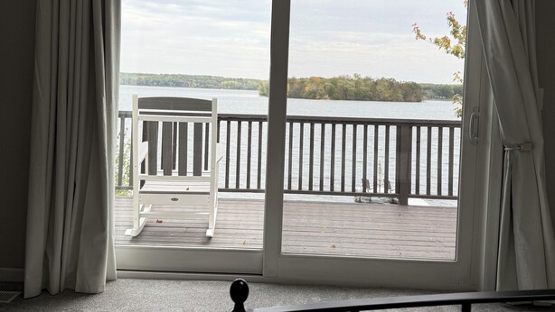 A room with a large sliding glass door leading to a balcony with a view of a lake and trees. - HAVEN COTTAGE - Close to Mpls, Far From Your Routine-FREE SUPS on Lake Fremont! (Zimmerman)