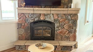 A living room with a stone fireplace, a television mounted above it, and a comfortable seating area with a sofa and a small table. - HAVEN COTTAGE - Close to Mpls, Far From Your Routine-FREE SUPS on Lake Fremont! (Zimmerman)
