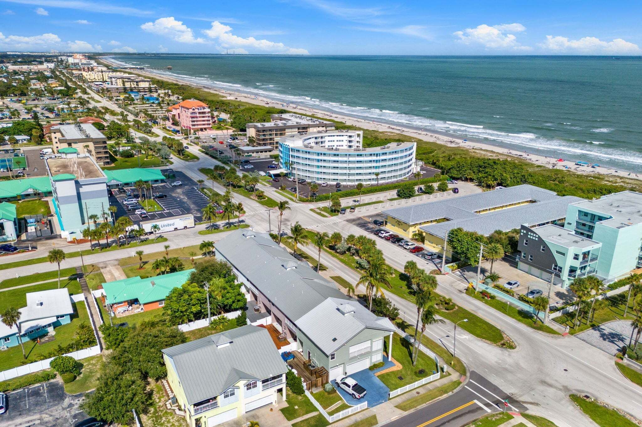 Luftaufnahme einer Küstenstadt mit Strandhotel, Straßen und Grünflächen.
