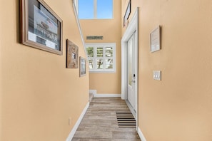 A narrow hallway with wooden flooring, a welcome sign, a door with a window, and framed pictures on the walls. - 3811 Ocean Beach Blvd (Cocoa Beach)