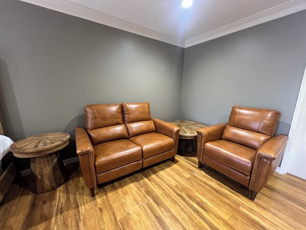 A room with a brown leather sofa, a round wooden coffee table, and a small wooden stool.