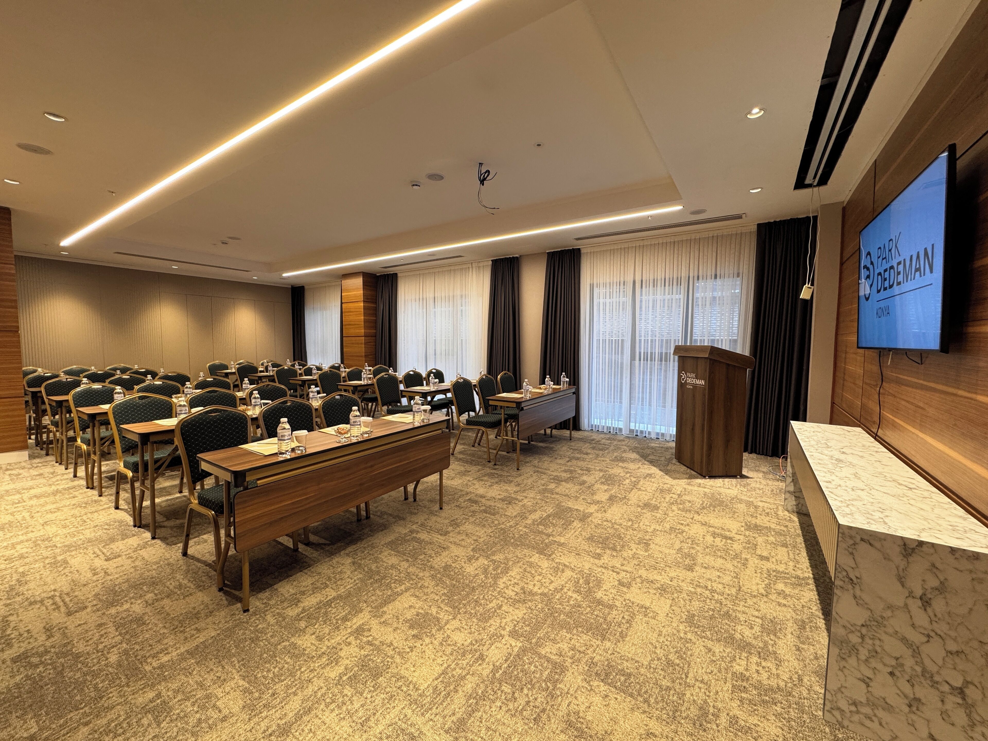 A conference room with a long table, chairs, a podium, and a television screen.
