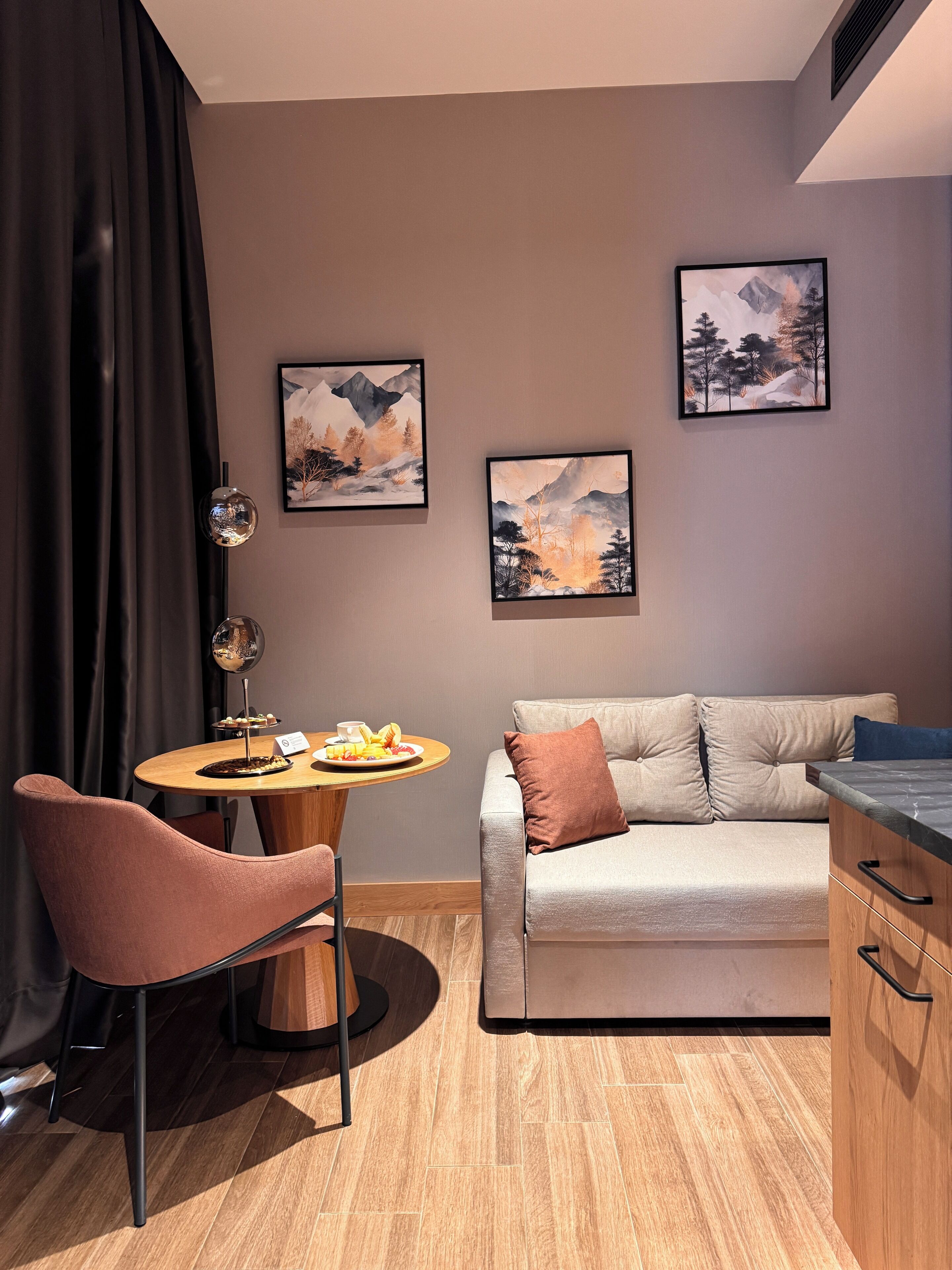 Una habitación moderna con un sofá, una mesa de comedor con una silla y dos cuadros de paisajes en la pared.