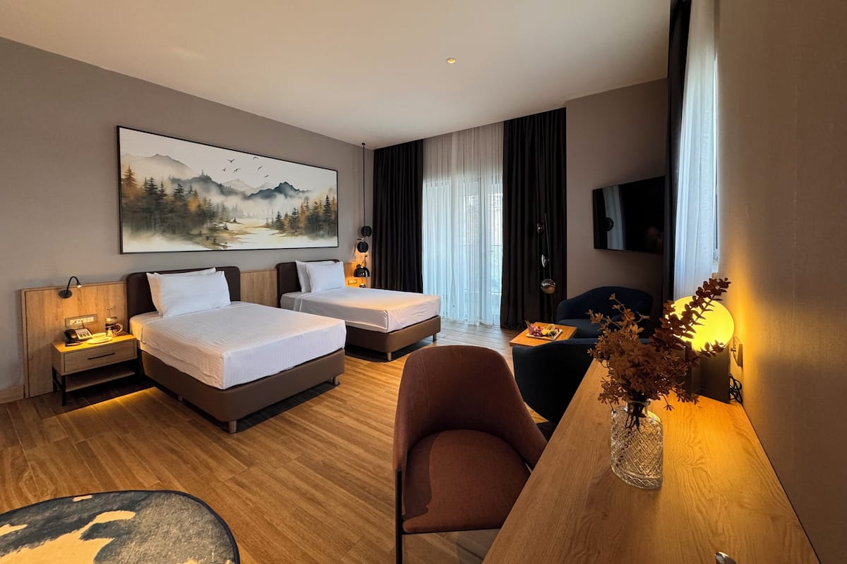 A hotel room with two beds, a desk with a vase, a chair, a TV, and a painting on the wall.