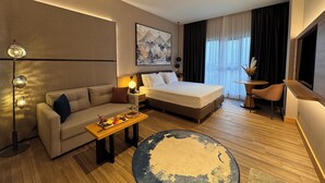 Ein modernes Hotelzimmer mit Bett, Sofa, Schreibtisch und einem großen Fenster mit Vorhängen.