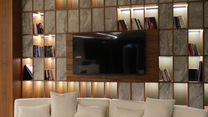 Ein modernes Wohnzimmer mit einem Ecksofa, einem Flachbildfernseher an einer Marmorwand und integrierten Bücherregalen mit Büchern.