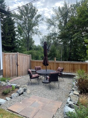 A patio with a round table and chairs, surrounded by a wooden fence, with trees and a clear sky in the background. - Downtown Snohomish - River Views - Walk to Town (Snohomish)