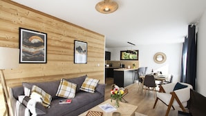 Ein modernes Wohnzimmer mit einer Holzwand, einem Sofa, einem Couchtisch und einem Essbereich mit einer Küche im Hintergrund.