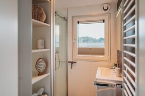 Et moderne badeværelse med et glasbadeværelsesafskærmning, et vindue med udsigt og en hvid vask med et håndklæde.