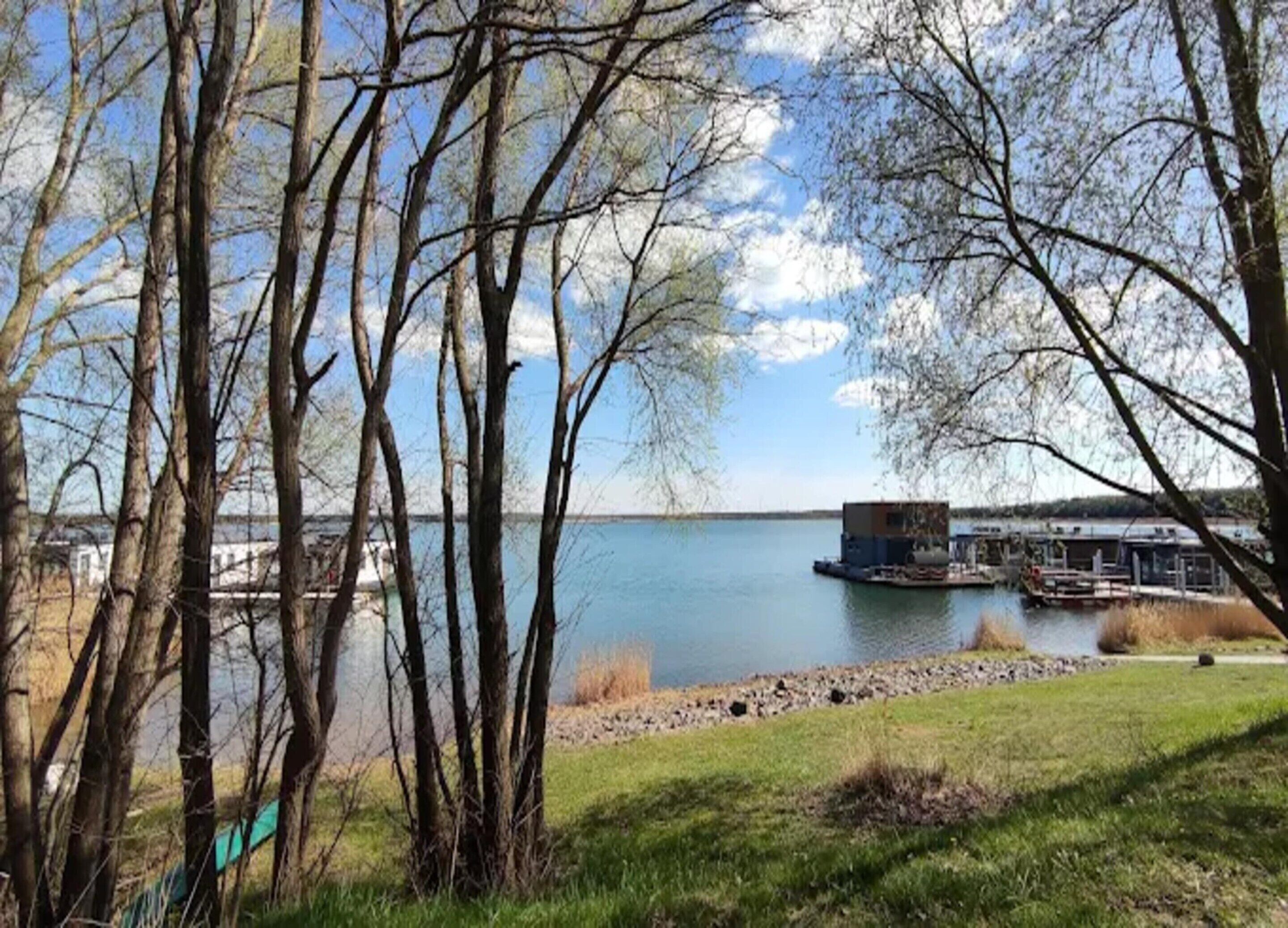 A lakeside property with a dock and a small building, surrounded by trees and a grassy area.