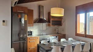 Una cocina moderna con un refrigerador de acero inoxidable, horno empotrado y estufa a gas. Hay una mesa de comedor dispuesta con platos y vasos.