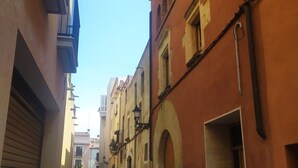 Una estrecha calle flanqueada por edificios con ventanas y puertas arqueadas, bajo un cielo azul despejado.