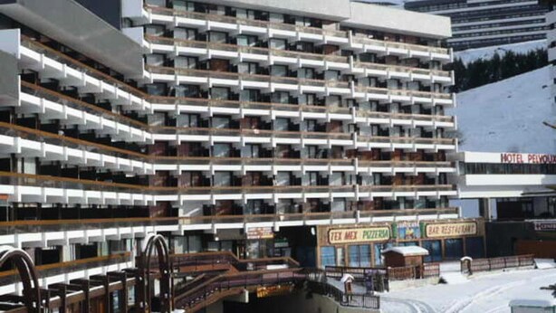 Un hotel de varios pisos con balcones, un telesilla y letreros para una pizzería y un café.