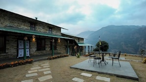 Ein Gebäude aus Stein mit einer grünen Markise, einer Außenbestuhlung und Blick auf die Berge.