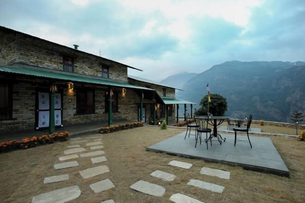 A stone building with a green awning, outdoor seating area, and a view of mountains. - Mountain Lodges of Nepal - Landruk (Lumle)