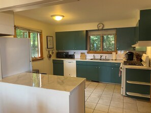 Een kleine keuken met blauwgroene kastjes, een witte koelkast, een magnetron, een spoelbak en een fornuis.