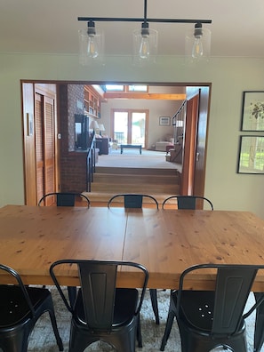 A dining area with a wooden table and chairs, a kitchen in the background, and a staircase leading to another level. - Lakefront 4-Bedroom Home on Lake Champlain with Stunning Views (Isle La Motte)