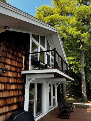 A two-story house with a balcony, large windows, and a wooden deck. - Lakefront 4-Bedroom Home on Lake Champlain with Stunning Views (Isle La Motte)