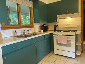 A kitchen with teal cabinets, a white stove, and a window with blinds. - Lakefront 4-Bedroom Home on Lake Champlain with Stunning Views (Isle La Motte)