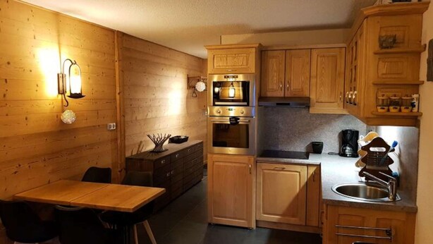 A compact kitchen with wooden cabinets, a double oven, and a sink. - Completely Renovated Studio Balcony Covered Parking (Araches-la-Frasse)