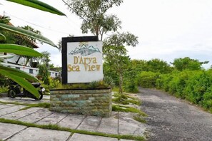 A sign for 'D'Arya Sea View' with a mountainous illustration, a stone planter, and a paved path leading to a lush green area. - Darya Sea View (Bali)