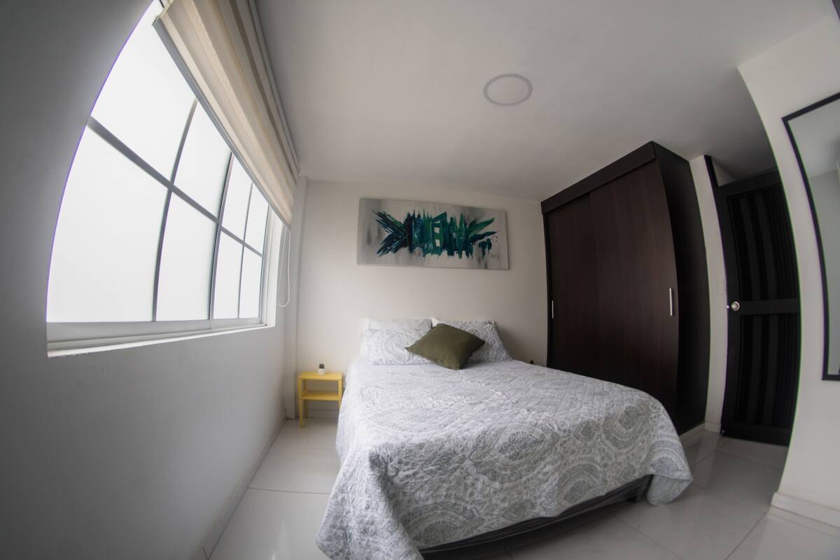 A bedroom with a bed, a nightstand, a window, and a door.