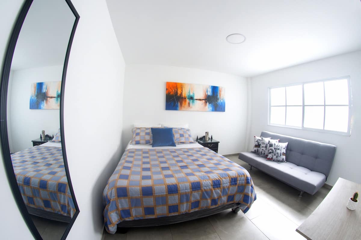 A modern bedroom with a large bed, a sofa, a mirror, and two abstract paintings on the wall.